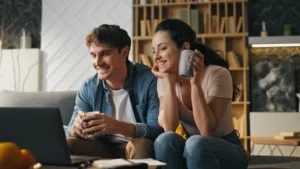 a Caucasian man and woman couple smiling and looking at a laptop participating in a couples Kousouli Neural Emotive Reprogramming KNER session with Dr. Kousouli